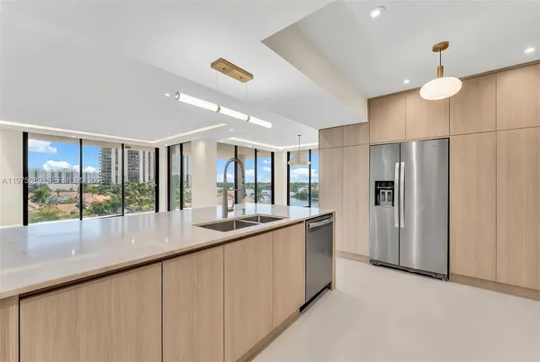 a large kitchen with kitchen island a large window a refrigerator and stainless steel appliances