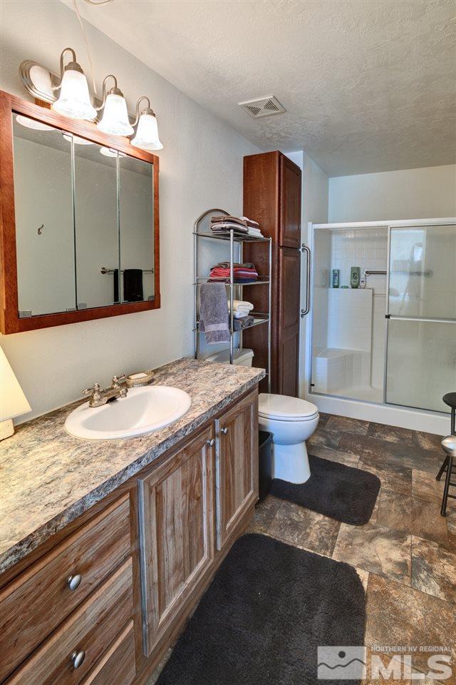 5954 Workman Road Fallon, NV 89406 - Photo 13 of 21 a bathroom with a granite countertop sink a toilet a mirror and shower