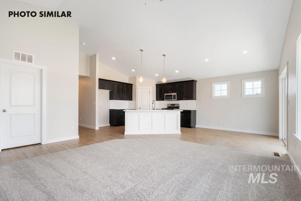 1708 Rapid Road Emmett, ID 83617 - Photo 7 of 33 Open-concept living area with vaulted ceilings, wood-finish flooring, and a kitchen featuring dark cabinetry, white countertops, and a white island