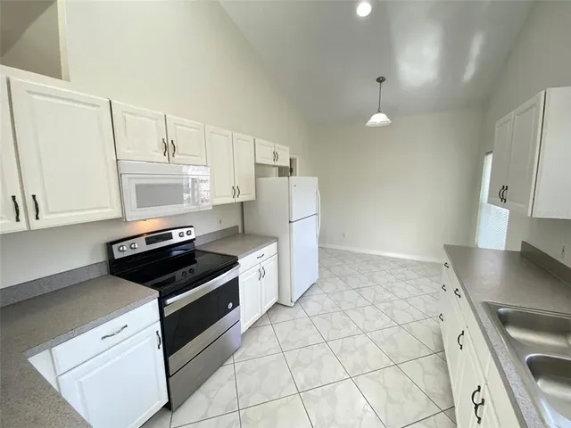 a kitchen with granite countertop a refrigerator a sink and white cabinets