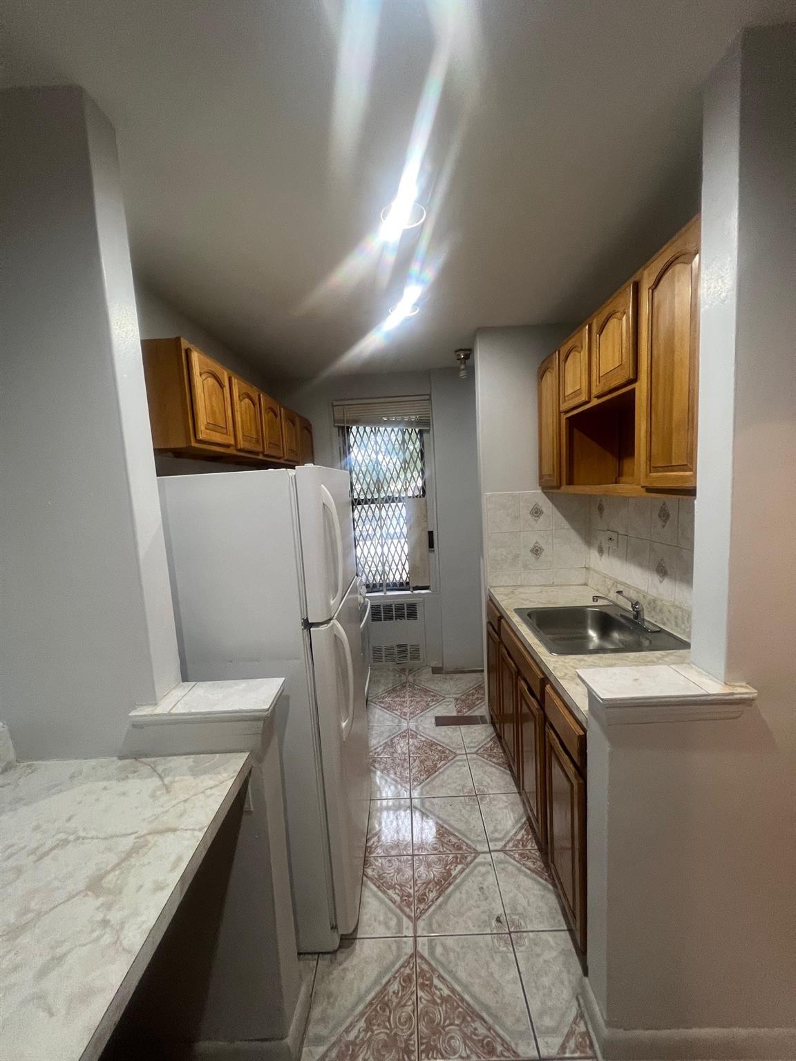 285 East 35th Street, Unit 2D Brooklyn, NY 11203 - Photo 12 of 21 Kitchen featuring light tile patterned floors, freestanding refrigerator, radiator heating unit, backsplash, and brown cabinets