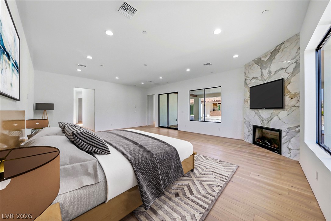 1140 Julie Road Henderson, NV 89002 - Photo 69 of 71 A spacious primary bedroom features rich wood flooring and a modern marble-clad fireplace, perfect for relaxation.