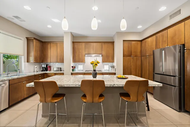 a kitchen with stainless steel appliances granite countertop a refrigerator a sink a stove a dining table and chairs