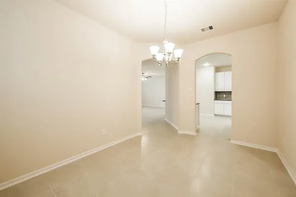 en empty room with chandelier fan and kitchen view