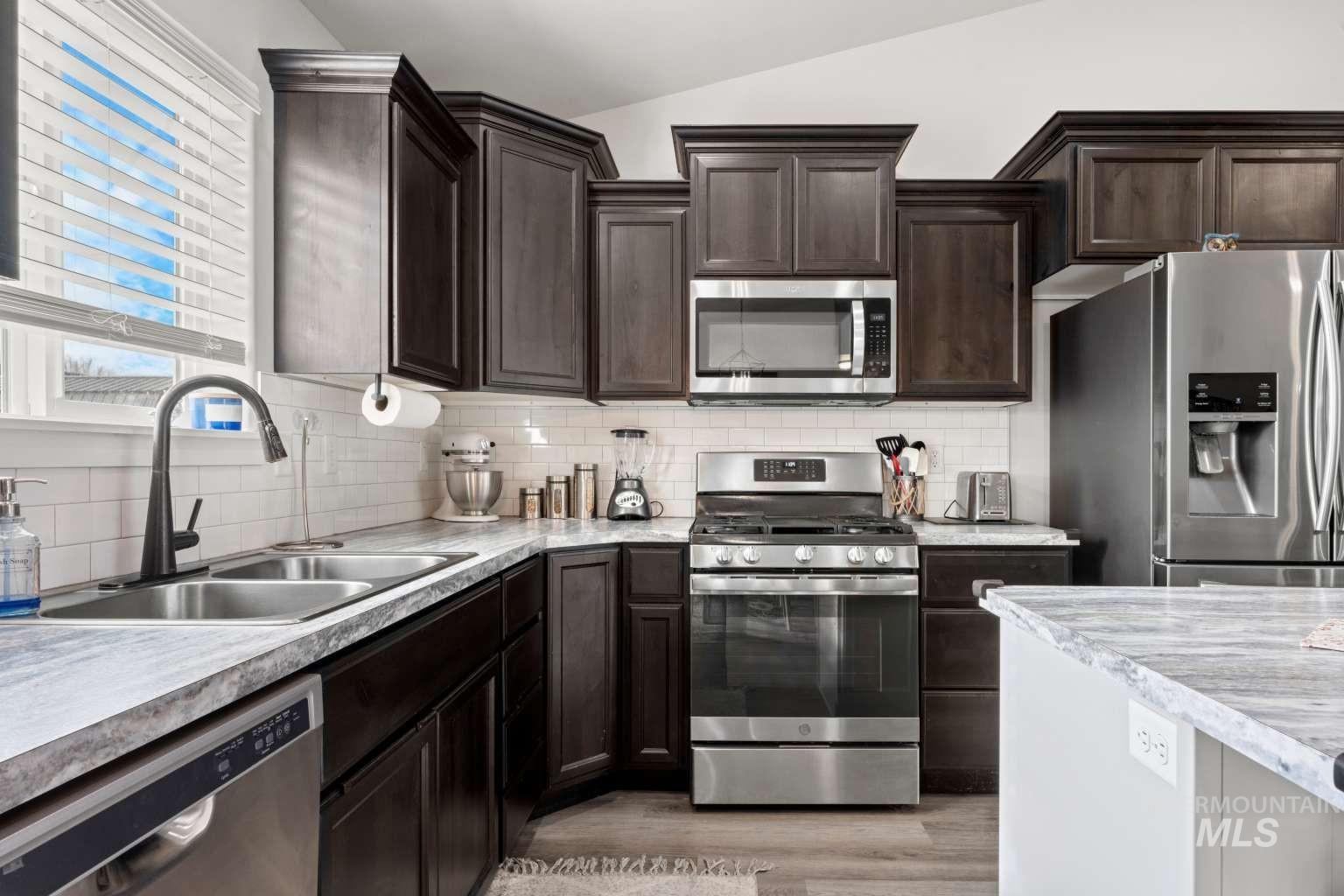 521 East 15th Street Rupert, ID 83350 - Photo 10 of 21 Kitchen with appliances with stainless steel finishes, light countertops, dark brown cabinets, light wood-type flooring, and vaulted ceiling