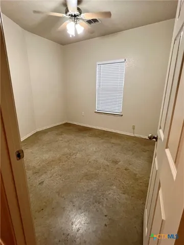 an empty room with a chandelier fan and windows
