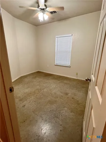 an empty room with a chandelier fan and windows