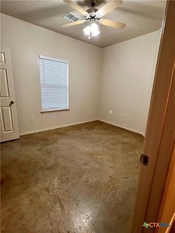 an empty room with a chandelier fan and windows
