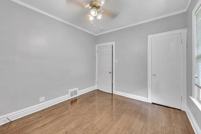 an empty room with wooden floor chandelier fan and windows