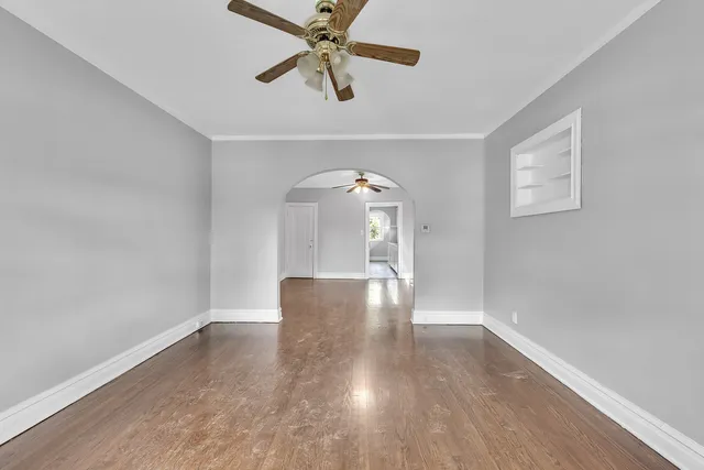 an empty room with wooden floor chandelier fan and windows