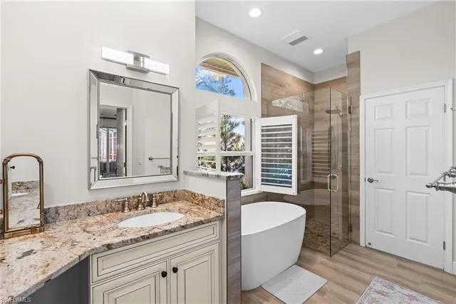a bathroom with a granite countertop sink mirror bathtub and next to a window
