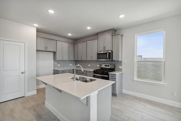 a kitchen with stainless steel appliances a sink a stove a refrigerator cabinets and a window