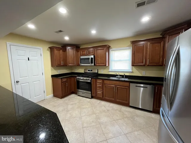 a kitchen with stainless steel appliances granite countertop wooden cabinets a refrigerator a sink a stove a microwave and island