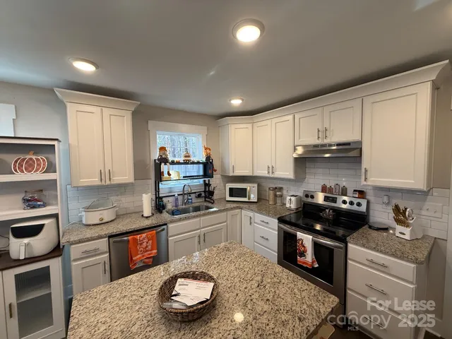 a kitchen with granite countertop a sink a stove a oven a counter space and cabinets