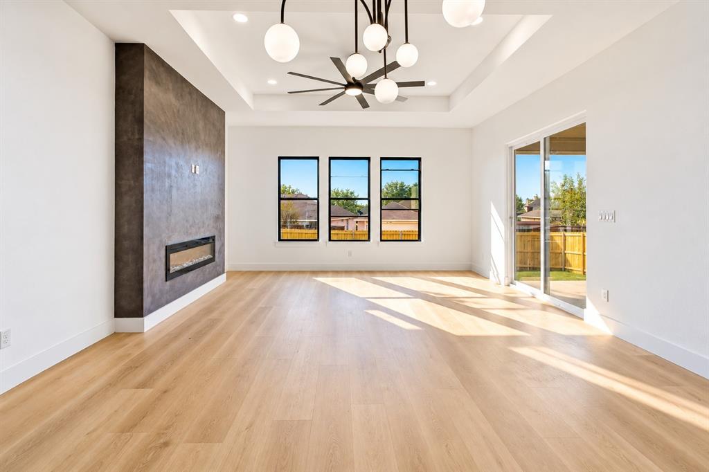 1640 West Wintergreen Road Lancaster, TX 75134 - Photo 8 of 37 Tray ceiling with recessed lighting and contemporary chandelier, wood-finish flooring, linear electric fireplace, three large windows, and sliding glass door