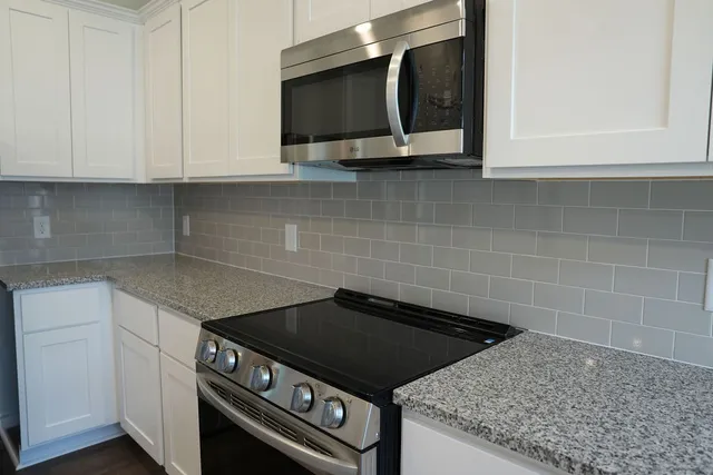 a kitchen with granite countertop a stove and a white cabinets