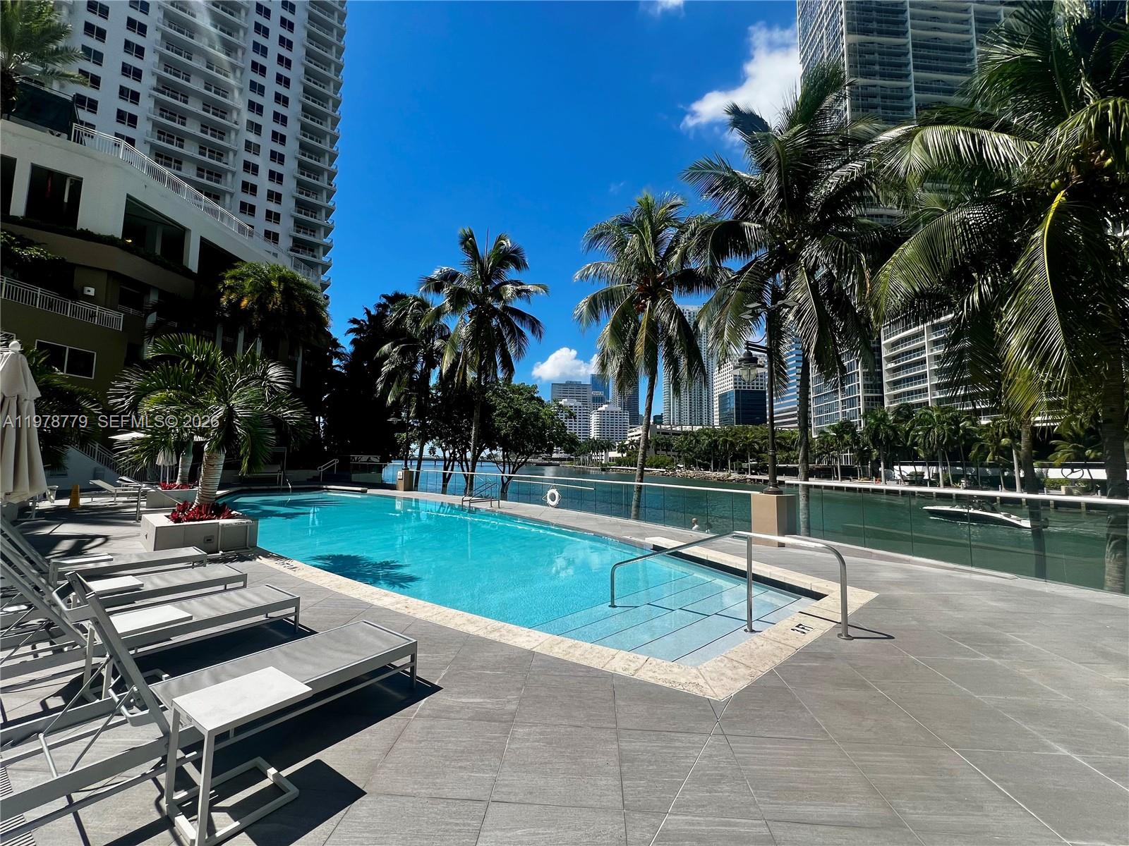 901 Brickell Key Boulevard, Unit 1001 Miami, FL 33131 - Photo 12 of 18 a view of a swimming pool with lounge chair and palm trees