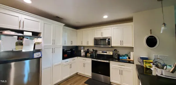 a kitchen with stainless steel appliances granite countertop a refrigerator a sink dishwasher and white cabinets with wooden floor