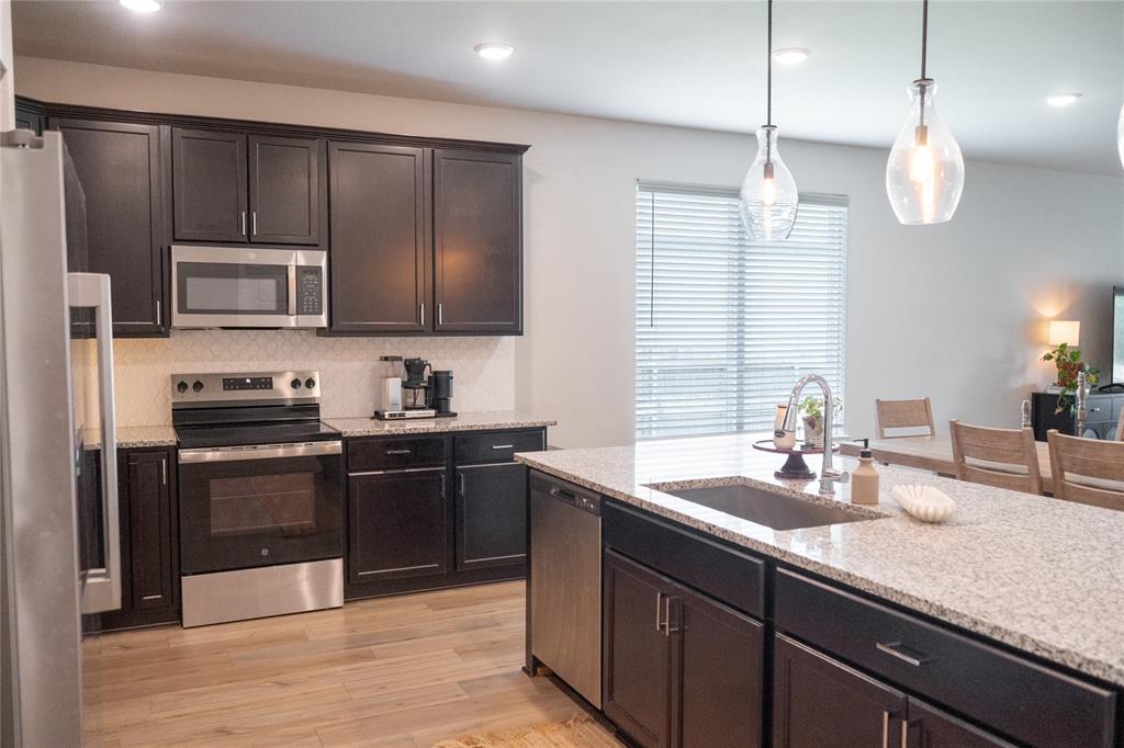 7909 Townsend Drive Waco, TX 76708 - Photo 6 of 22 Modern kitchen featuring dark wood cabinetry, stainless steel appliances, granite countertops, and wood-finish flooring