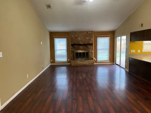 an empty room with wooden floor fire place and windows