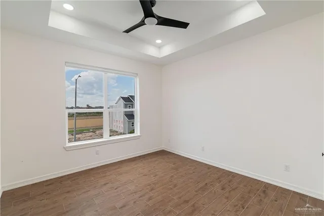 an empty room with wooden floor ceiling fan and windows