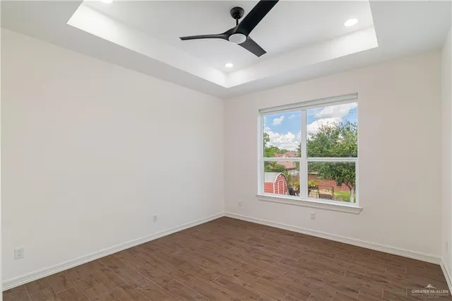 an empty room with wooden floor ceiling fan and windows
