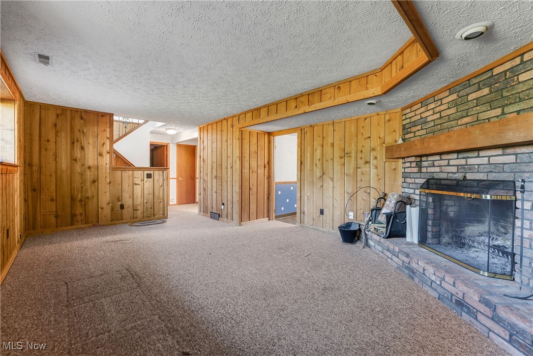 123 Boulder Ridge Place Painesville, OH 44077 - Photo 22 of 28 Unfurnished living room featuring a textured ceiling, carpet floors, a fireplace, and wooden walls