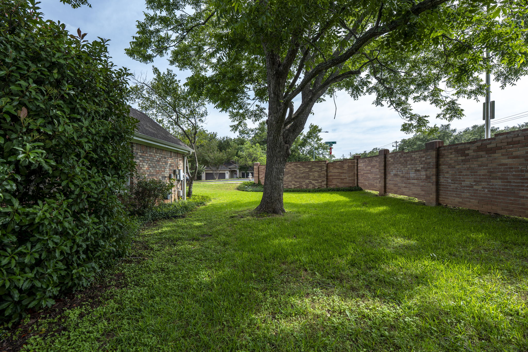 7172 Ridge Oak Road Austin, TX 78749 - Photo 3 of 40 A well-maintained side yard features a mature tree and a sturdy brick fence, providing privacy and verdant green space.