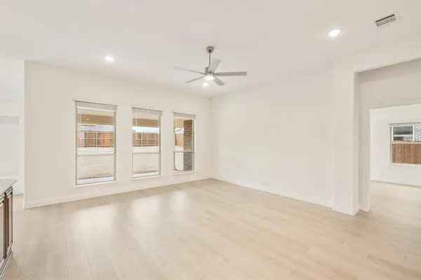 an empty room with wooden floor ceiling fan and windows