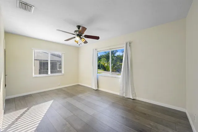 an empty room with wooden floor a ceiling fan and windows