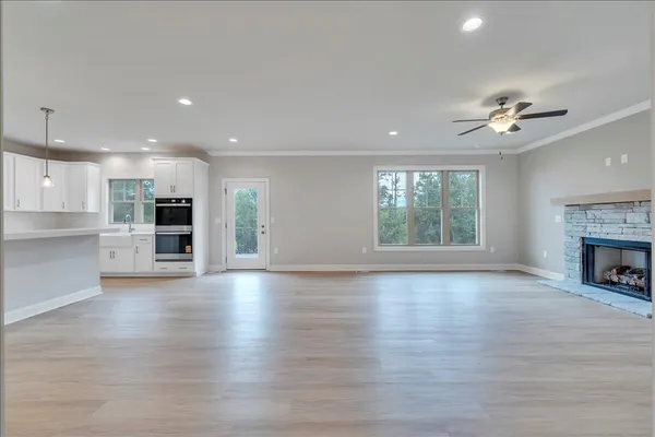an empty room with wooden floor fire place and kitchen view