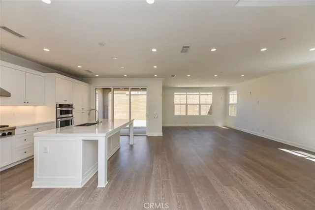 a view of kitchen with stainless steel appliances granite countertop a stove top oven a sink a refrigerator and white cabinets with wooden floor