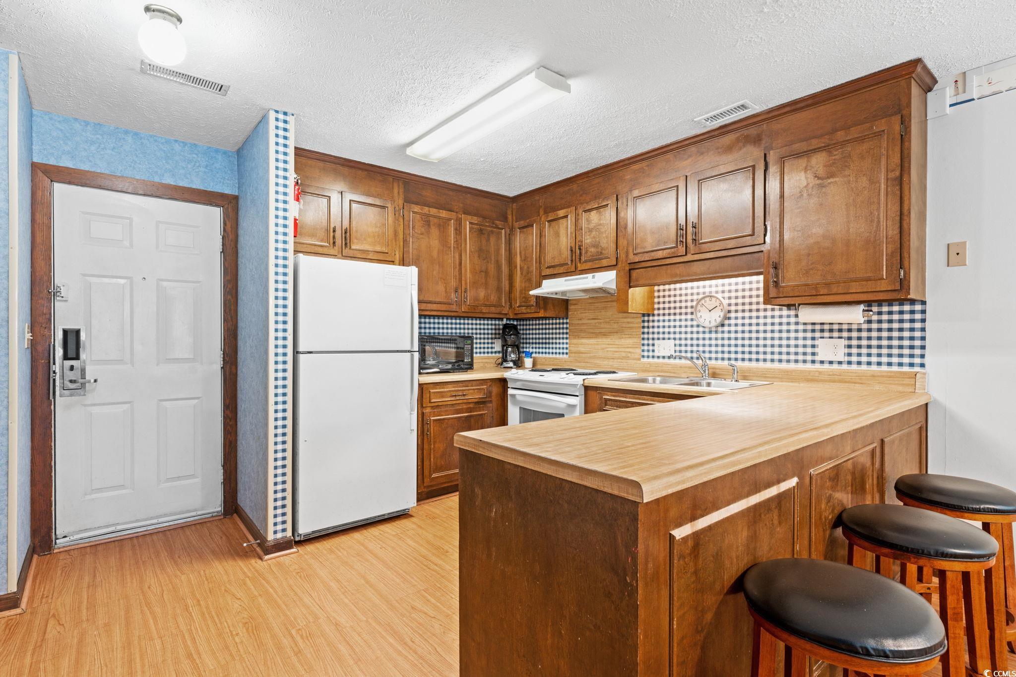 307 70th Avenue North, Unit 202 Myrtle Beach, SC 29572 - Photo 23 of 33 Kitchen with a peninsula, light countertops, a breakfast bar, brown cabinets, and a textured ceiling