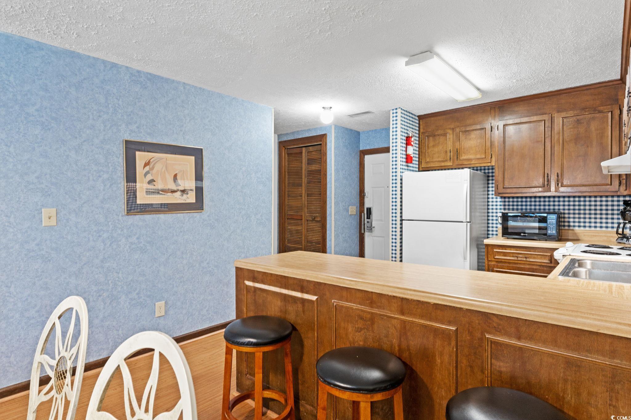 307 70th Avenue North, Unit 202 Myrtle Beach, SC 29572 - Photo 24 of 33 Kitchen with a kitchen breakfast bar, a peninsula, light countertops, freestanding refrigerator, and brown cabinets