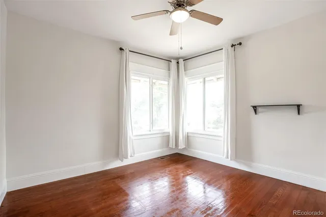 an empty room with wooden floor fan and windows