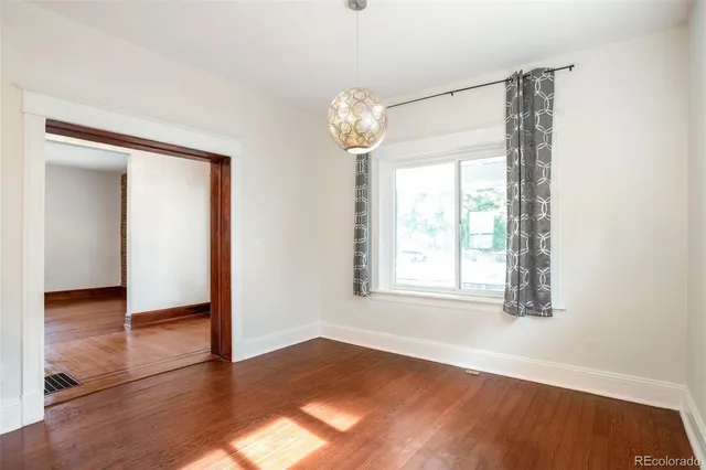 an empty room with wooden floor chandelier and windows