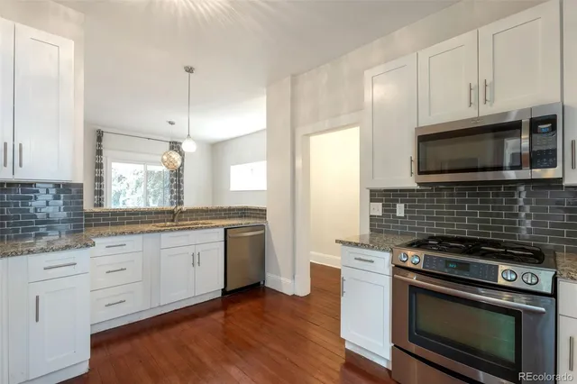 a kitchen with stainless steel appliances white cabinets granite counter tops and a window