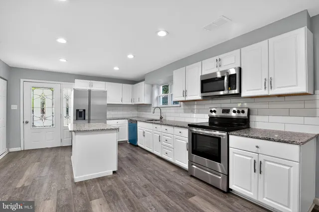 a kitchen with stainless steel appliances granite countertop a stove top oven a sink a refrigerator white cabinets and wooden floor