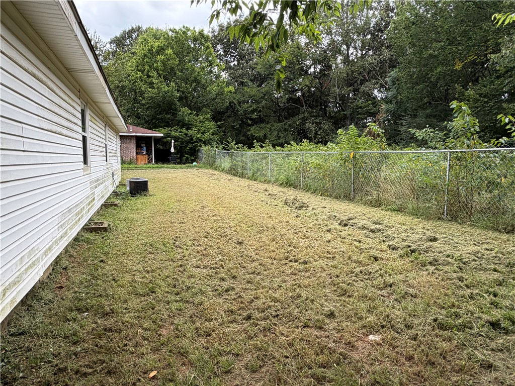 909 Riddell Street Clarksville, AR 72830 - Photo 26 of 26 Expansive side yard featuring a chain-link fence, mature trees, and a vinyl-sided exterior