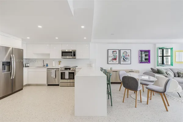 a living room with stainless steel appliances furniture a large window and a kitchen view