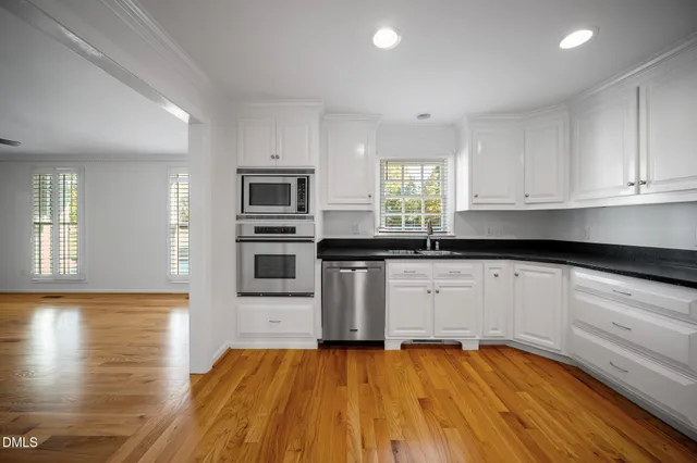 a kitchen with granite countertop wooden floors stainless steel appliances and sink