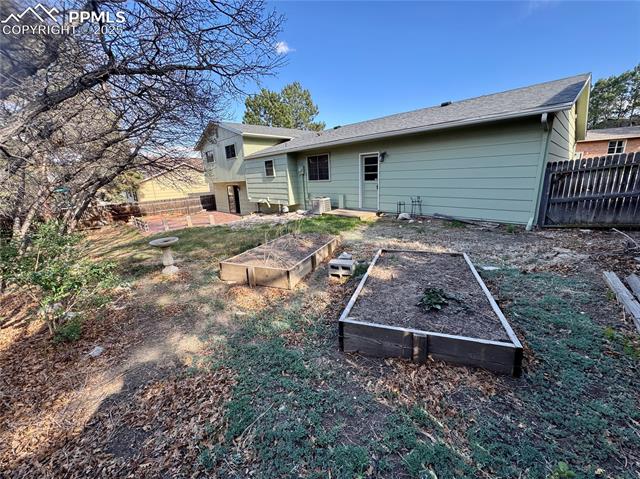 280 Raven Hills Road Colorado Springs, CO 80919 - Photo 5 of 48 Back of house featuring fence, a vegetable garden, and cooling unit