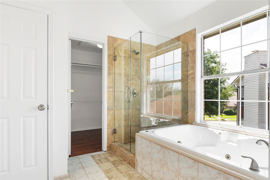 559 Raintree Circle Coppell, TX 75019 - Photo 34 of 40 Soaking tub with integrated jets and tiled surround, accompanied by a glass-enclosed shower with stone-finish tile