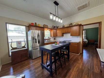 a kitchen with stainless steel appliances granite countertop a refrigerator a sink dishwasher a stove and a dining table with wooden floor