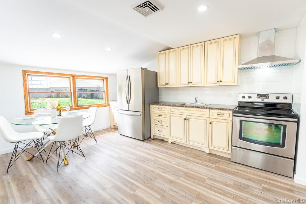 202 2nd Road Wappingers Falls, NY 12590 - Photo 12 of 24 Kitchen with appliances with stainless steel finishes, decorative backsplash, cream cabinetry, wall chimney exhaust hood, and dark stone countertops