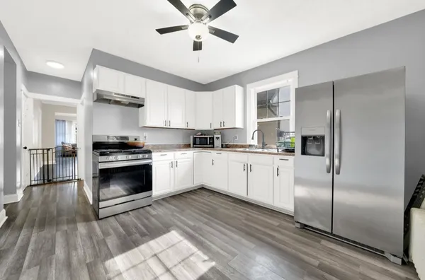 a kitchen with granite countertop a refrigerator a sink dishwasher a stove and white cabinets with wooden floor
