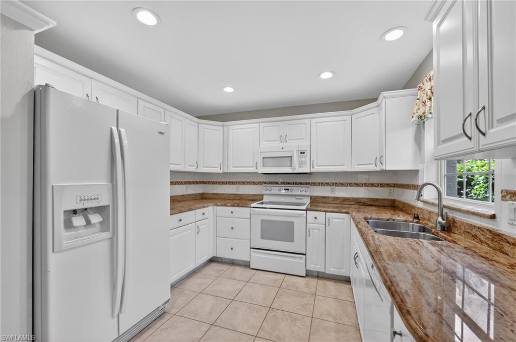 8534 Chase Preserve Drive Naples, FL 34113 - Photo 8 of 44 Kitchen featuring white appliances, white cabinetry, light stone counters, light tile floors, and tasteful backsplash