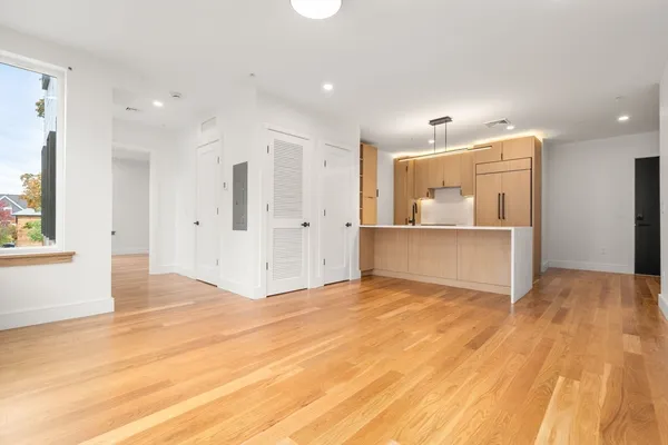 a view of an empty room with kitchen and window