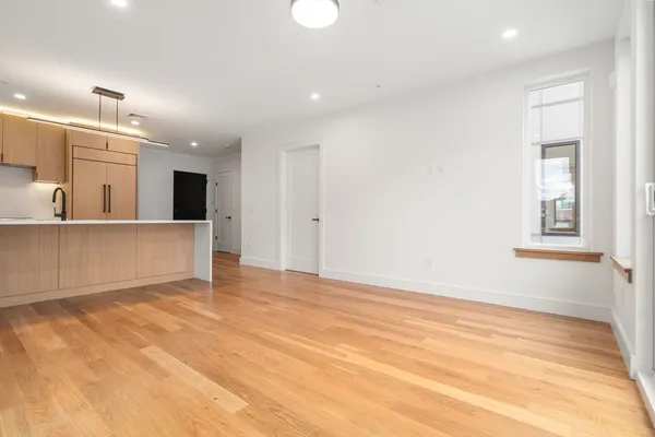 a view of an empty room with kitchen and window
