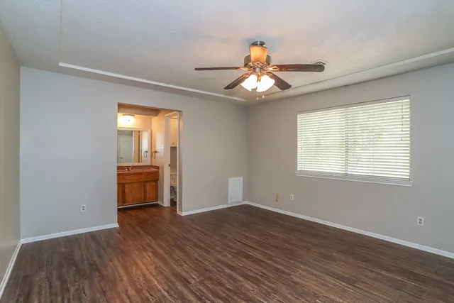 an empty room with wooden floor fan and windows